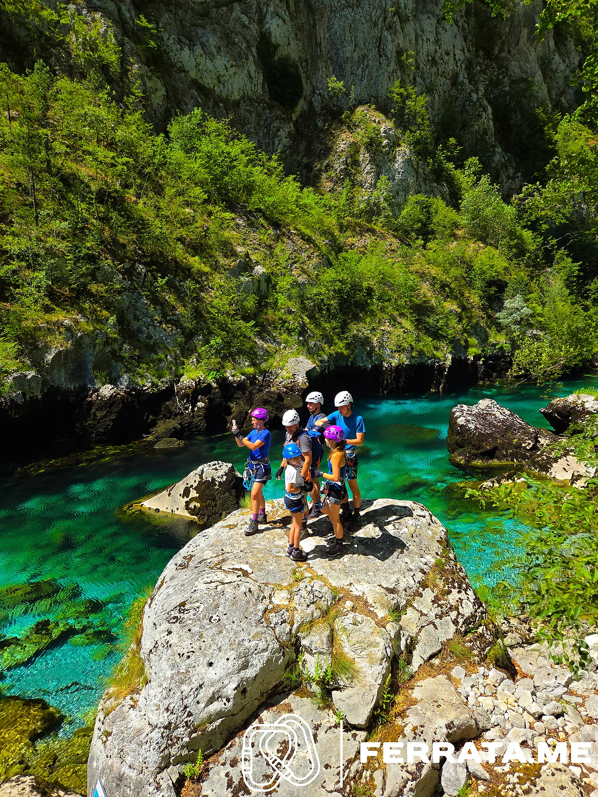A group in helmets standing on a boulder in the turquoise river.