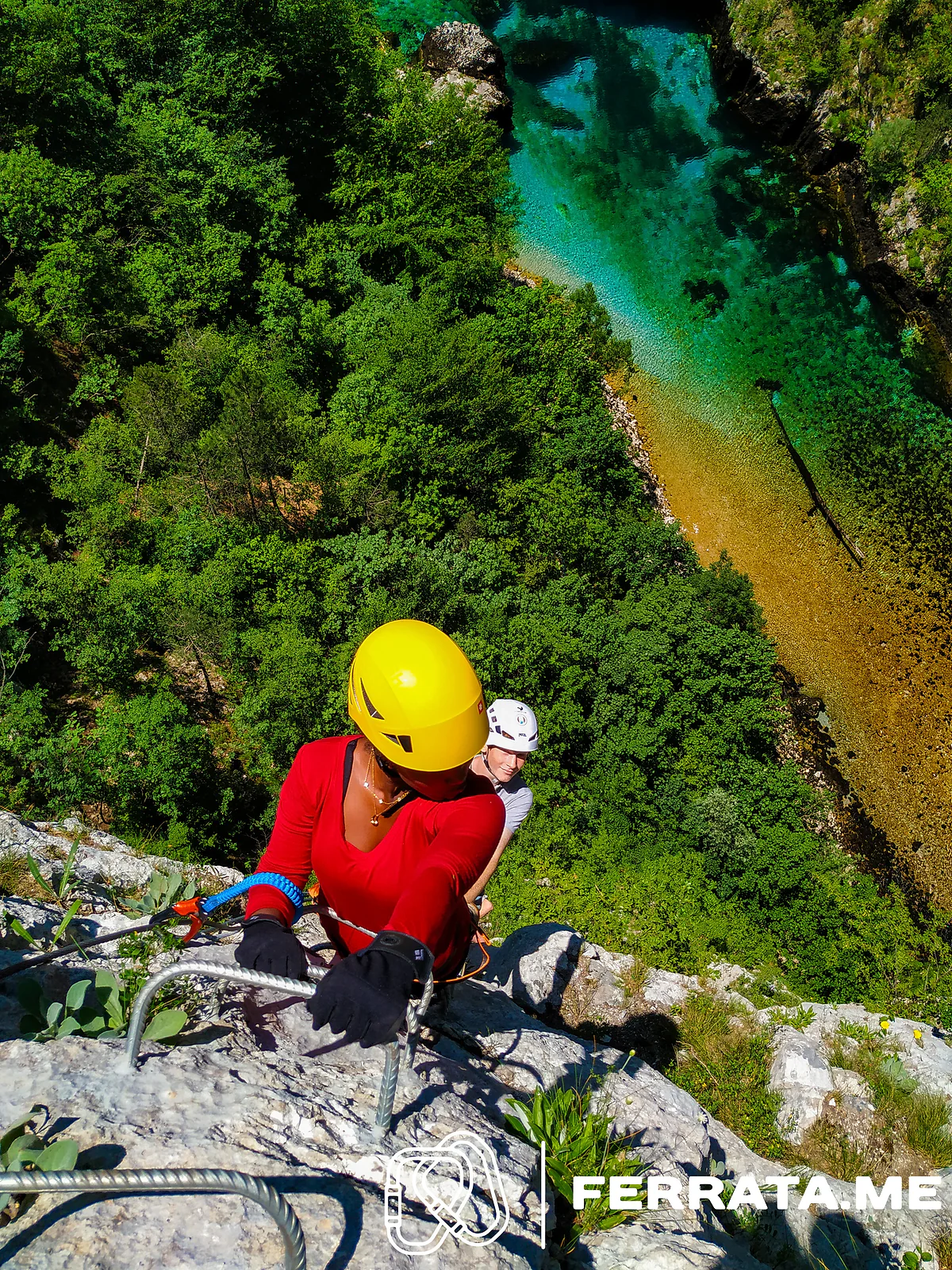 A climber in a yellow helmet and red shirt near the top of the wall, with the river far below.